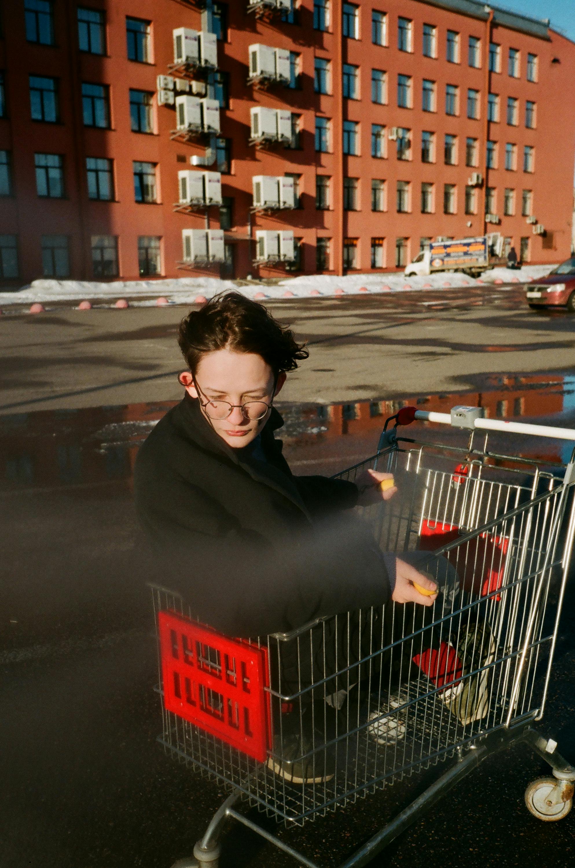阳光明媚的日子里，一个人坐在购物车里，背景是城市建筑