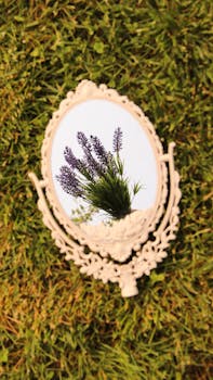 A vintage mirror on grass reflects blooming lavender flowers, creating a serene outdoor scene.