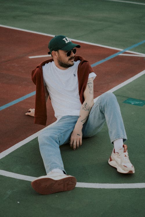 A man sitting on a basketball court with a hat on