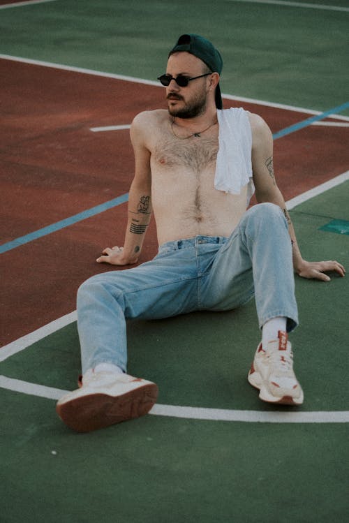 A shirtless man sitting on a basketball court