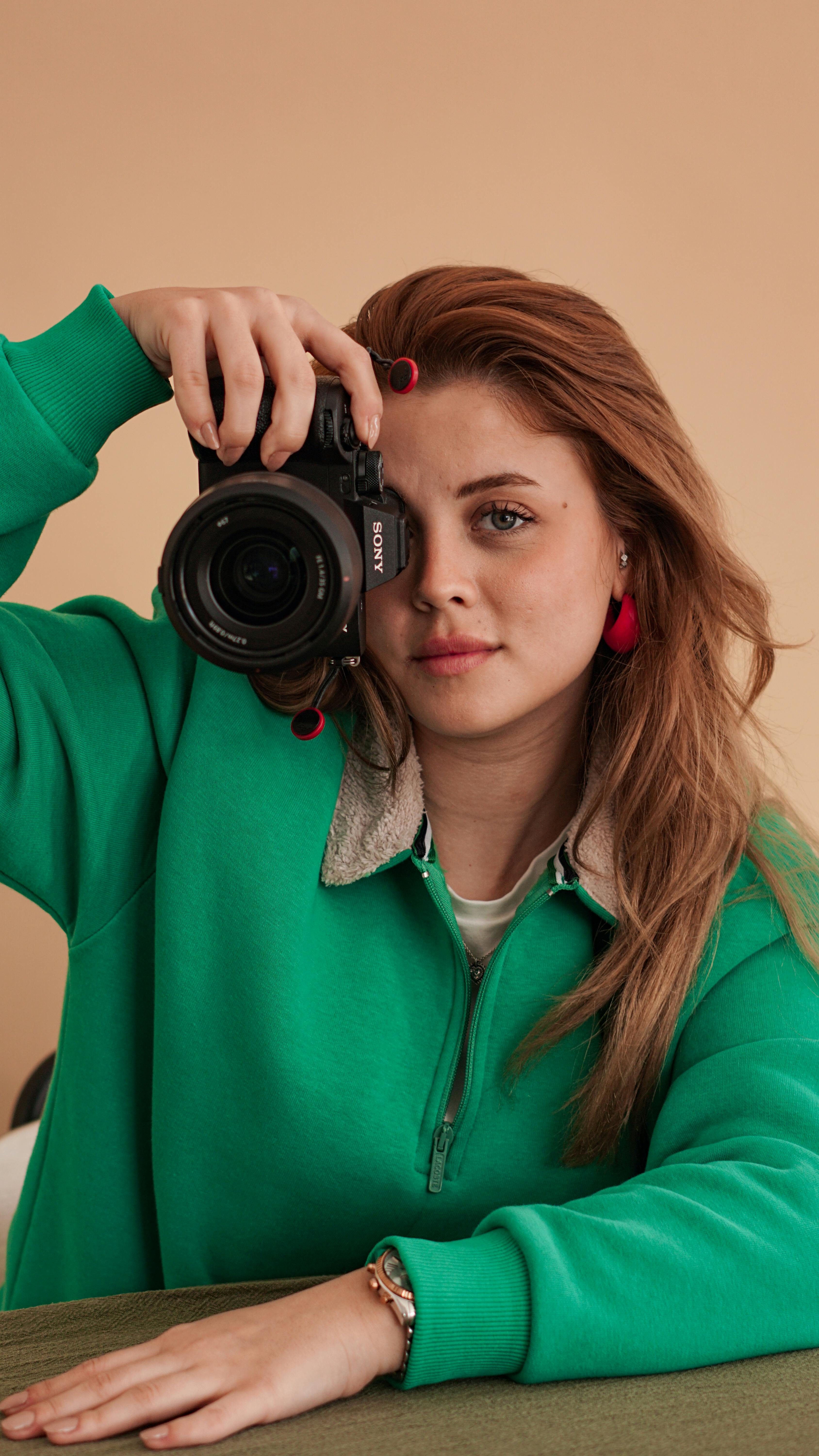 Woman posing with camera in a studio setting, wearing a green pullover.