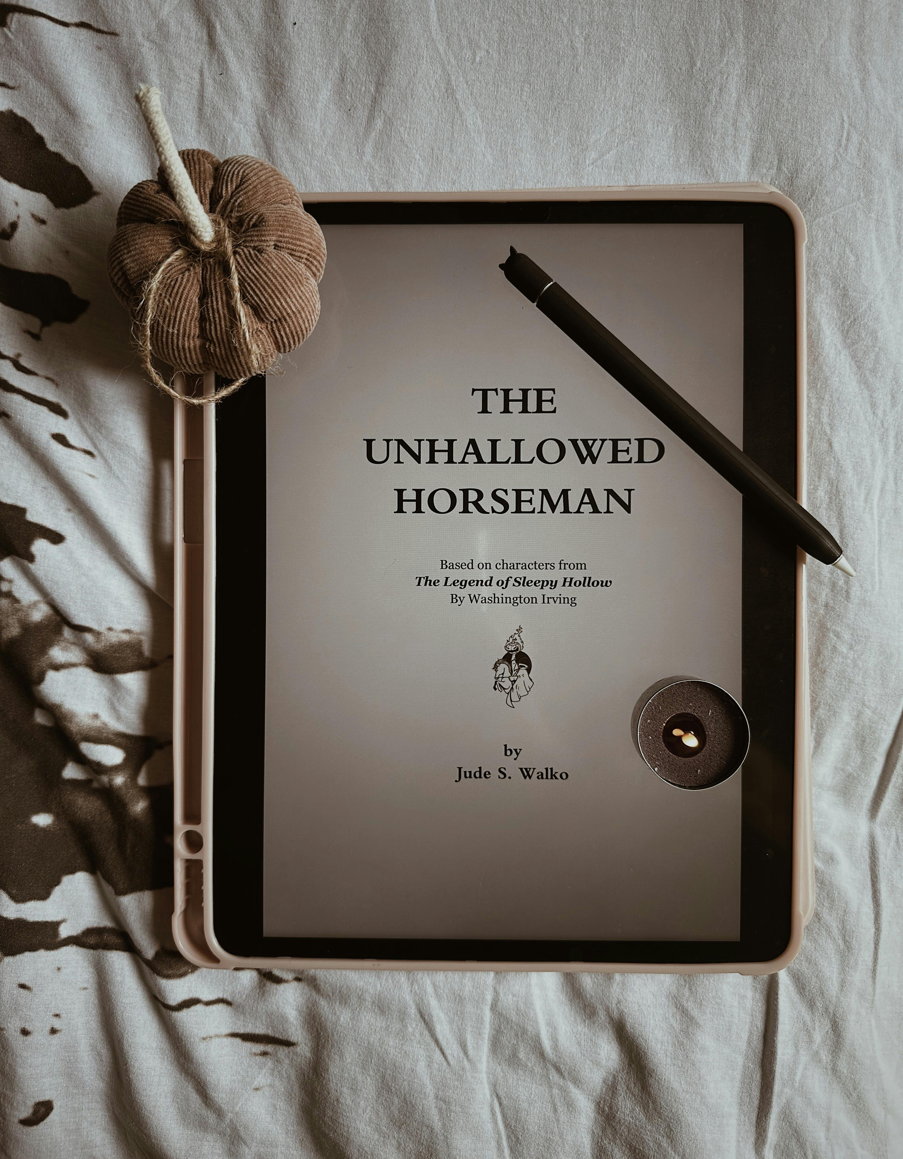 Tablet displaying 'The Unhallowed Horseman' book cover with candle and yarn for cozy aesthetics.