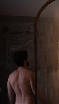 A man with short hair stands in a shower, seen from the back.