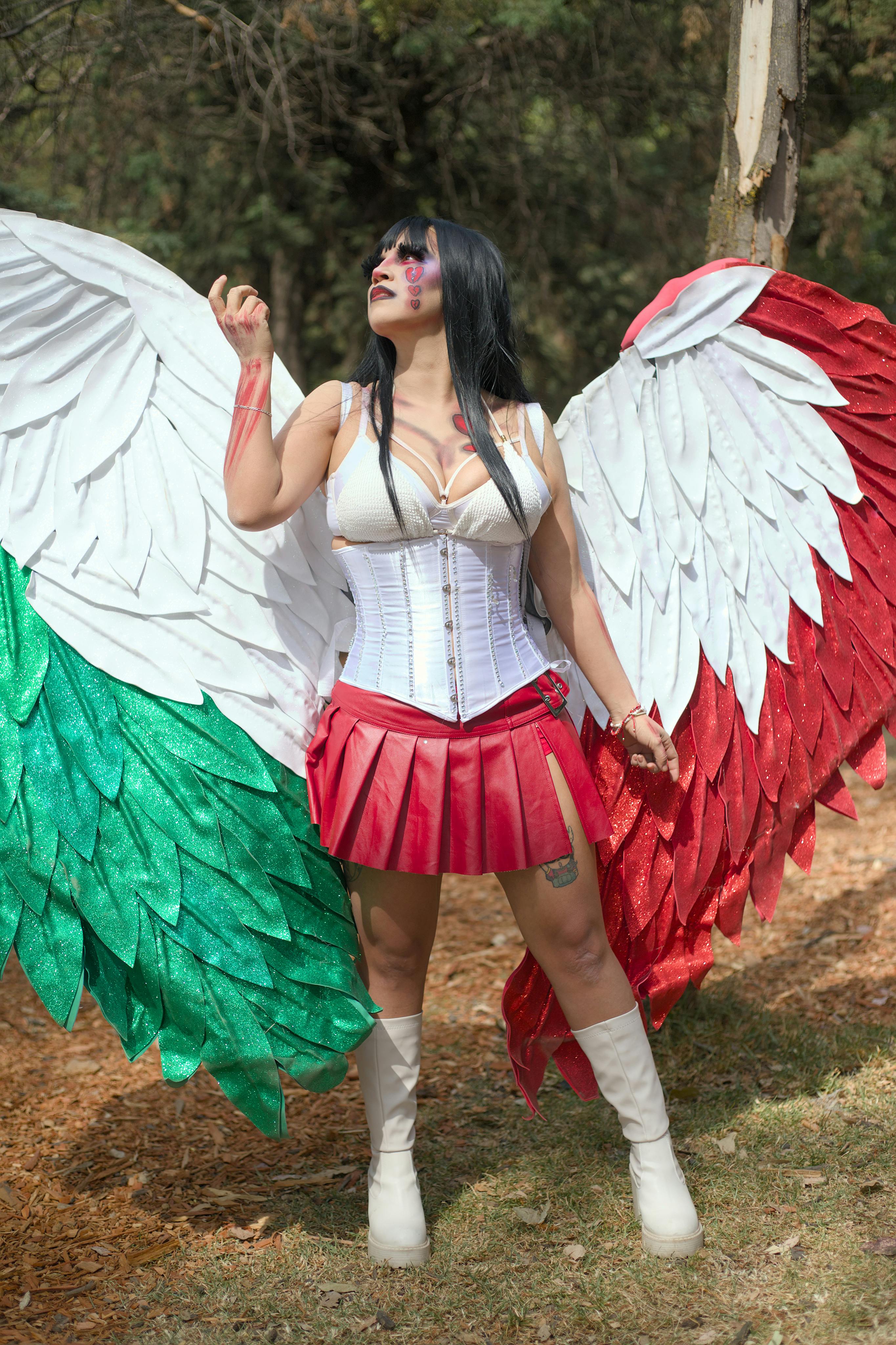 Woman in a vibrant angel costume with large, colorful wings standing in a forest setting.