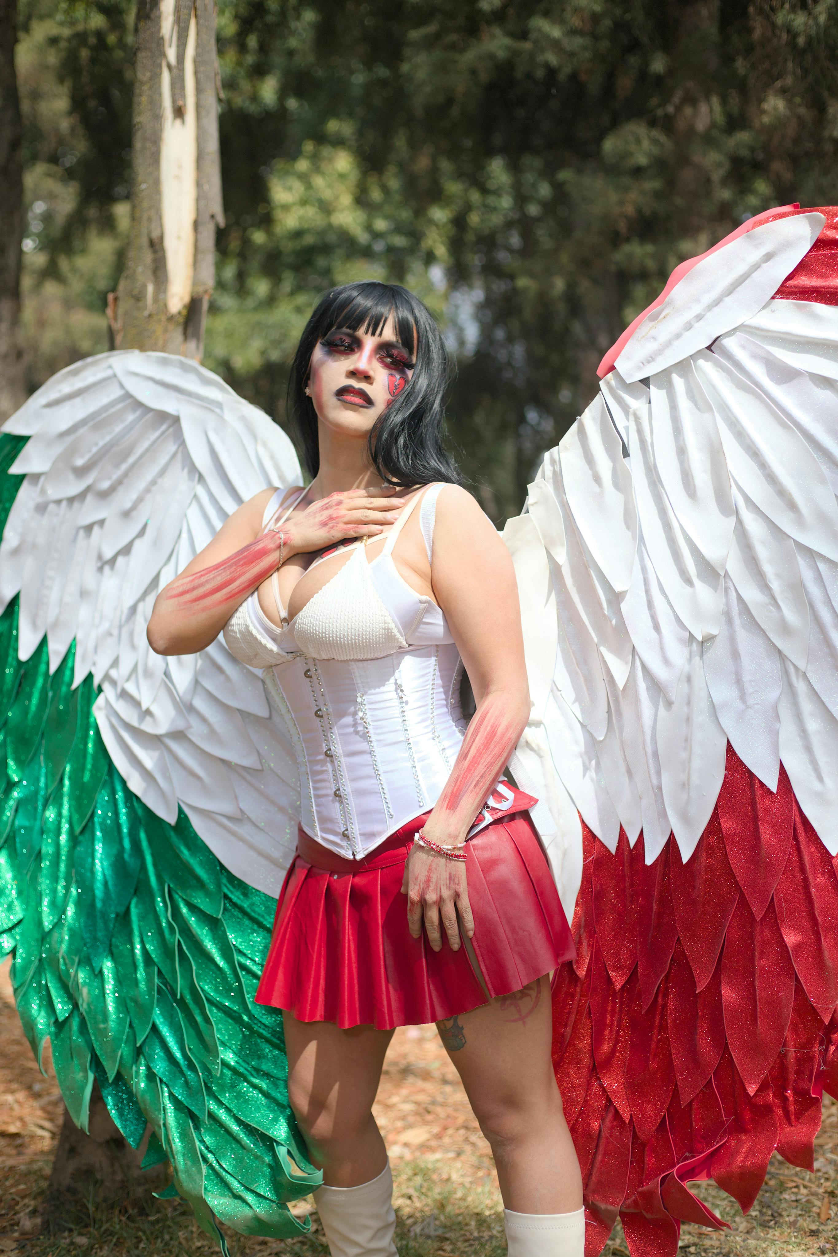 A woman in a Mexican flag-inspired angel costume posing outdoors with vibrant wings.