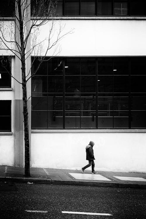 Man Walking near Building Wall in Black and White