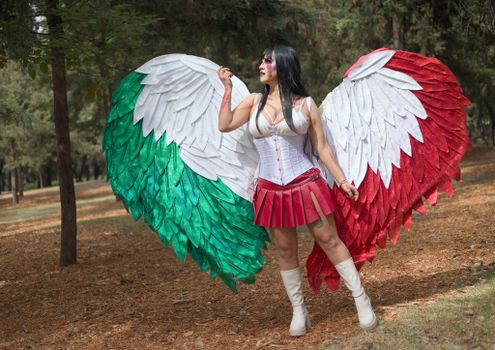 Woman in a forest wearing angel wings with Mexican flag colors, embracing cosplay.