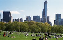 在纽约市天际线的背景下，人们在中央公园享受着阳光明媚的一天