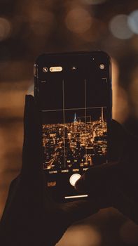 A smartphone captures the illuminated New York City skyline, focusing on the Empire State Building.