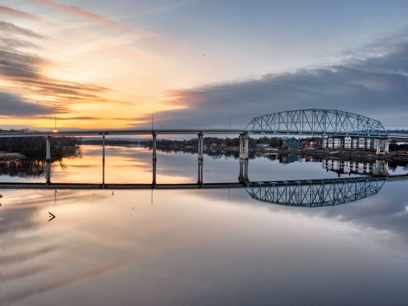 A long steel bridge reflected in a river at sunset