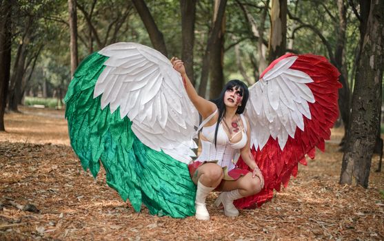 Woman in angel costume with Mexican flag colors in a wooded setting.