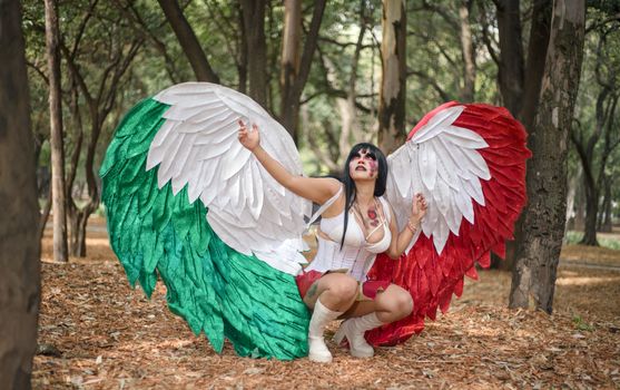 Woman in a vibrant cosplay costume poses in a forest setting, showcasing colorful wings.