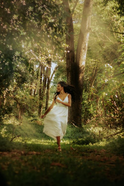 Free A woman in a white dress joyfully runs through a sunlit forest, embracing freedom and summer vibes. Stock Photo