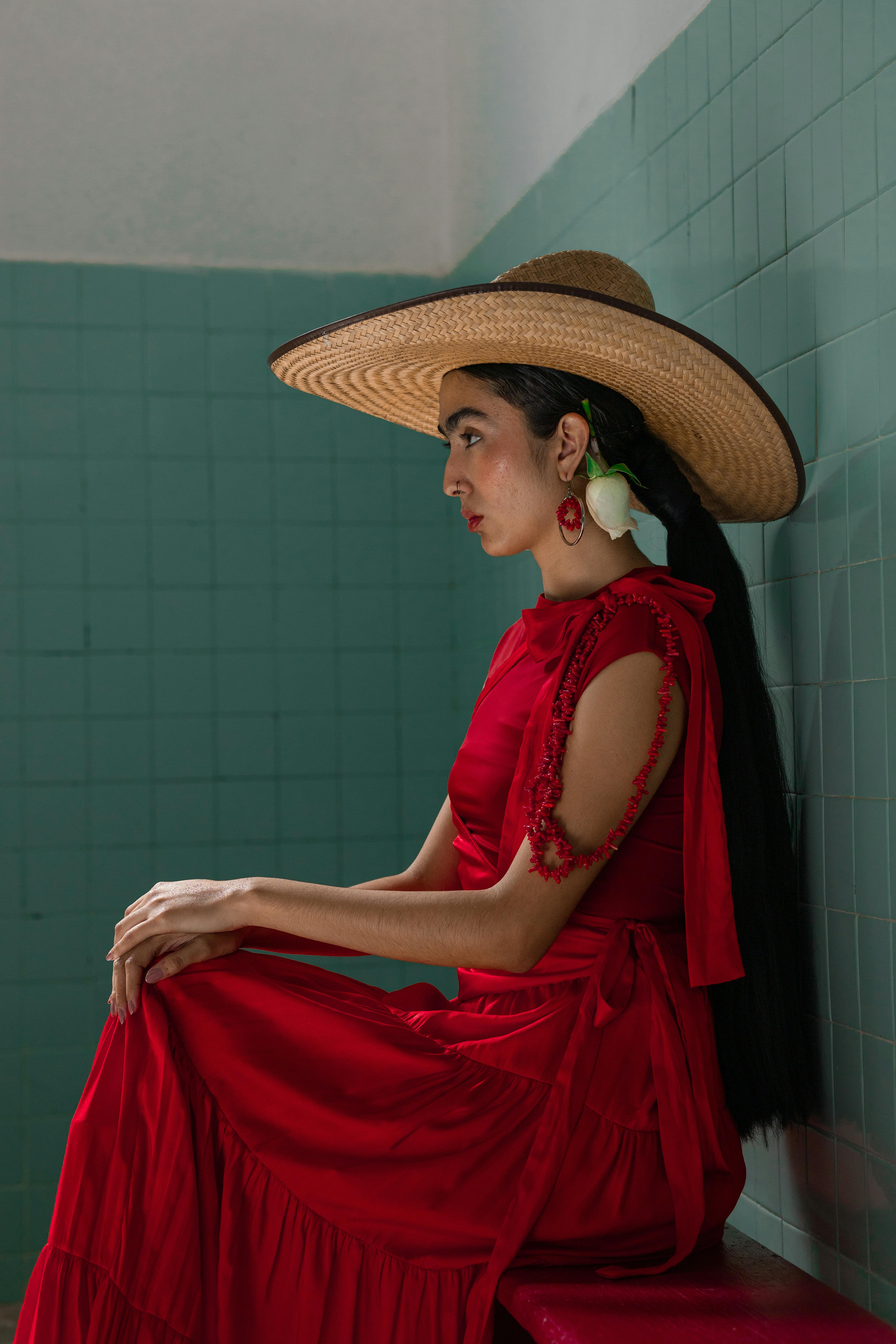 Stylish woman in a red dress with a wide-brimmed sombrero, captured in a serene indoor setting.