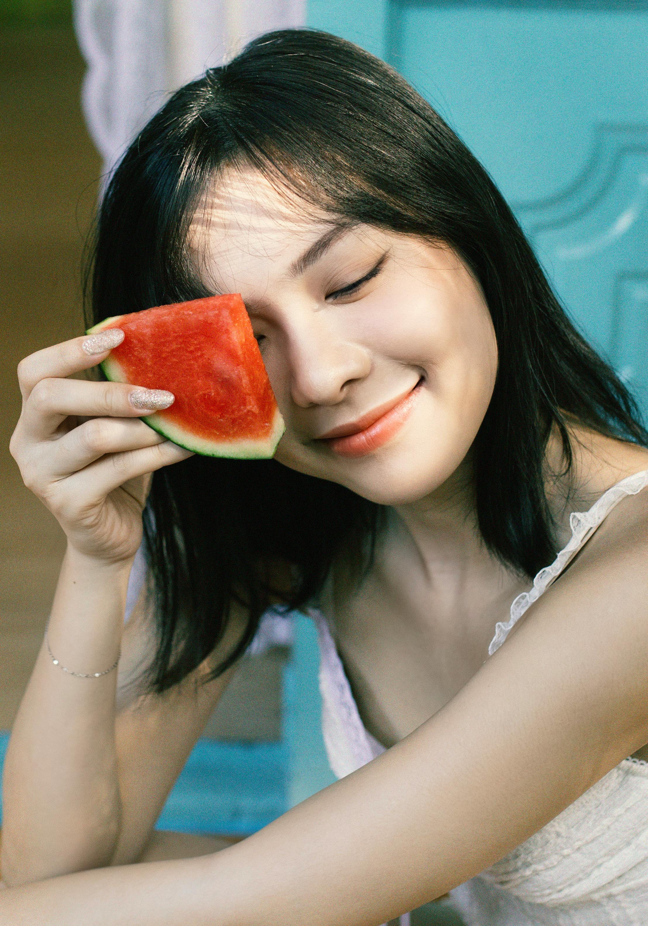Smiling woman with black hair enjoying a watermelon slice indoors.