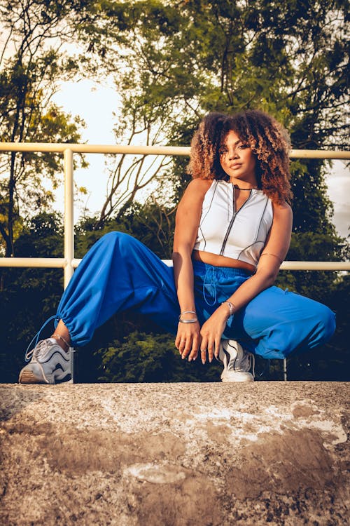A woman in blue pants and sneakers sitting on a ledge