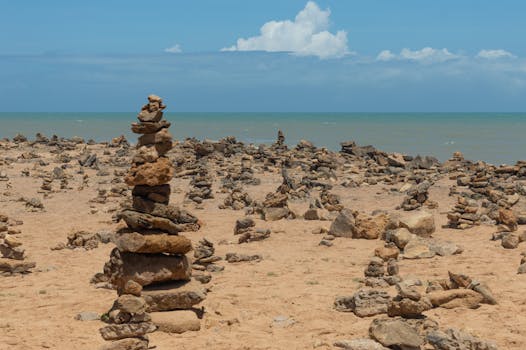 Peaceful beach with stone cairns against a clear blue sky and horizon.