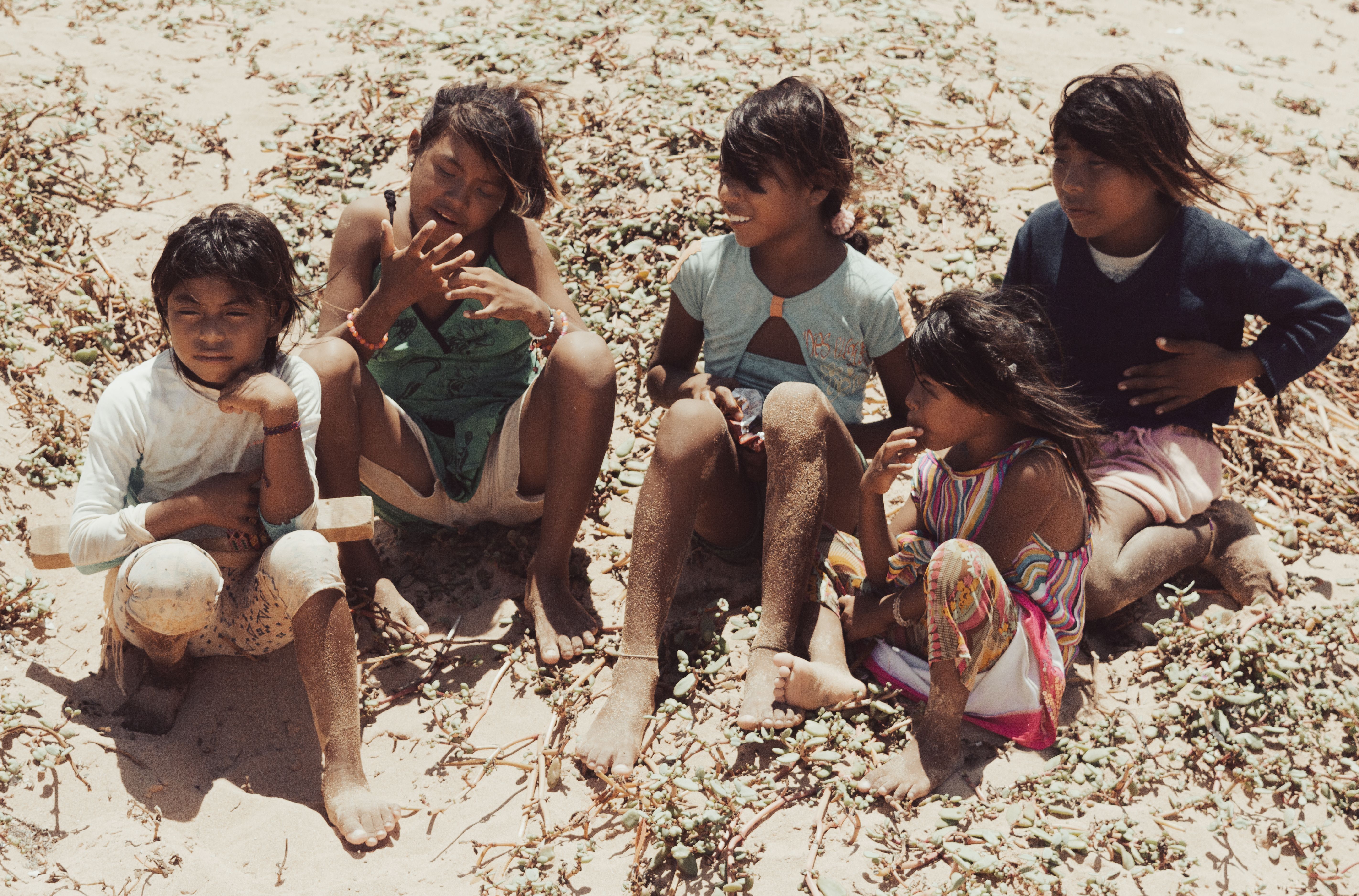 Five children sitting on the sandy beach, enjoying a sunny day together.