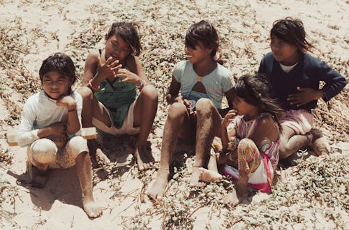A group of children sitting on the ground in the sand