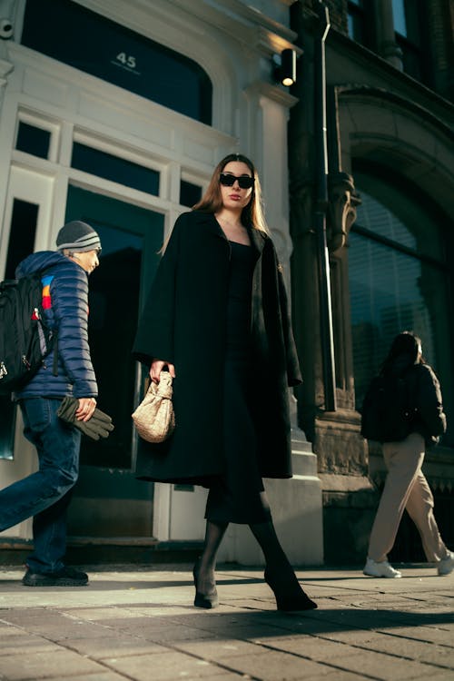 A woman in a black coat and sunglasses walking down a street