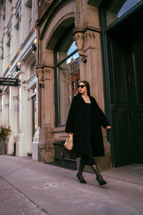 A woman in a black coat and black boots walking down the street