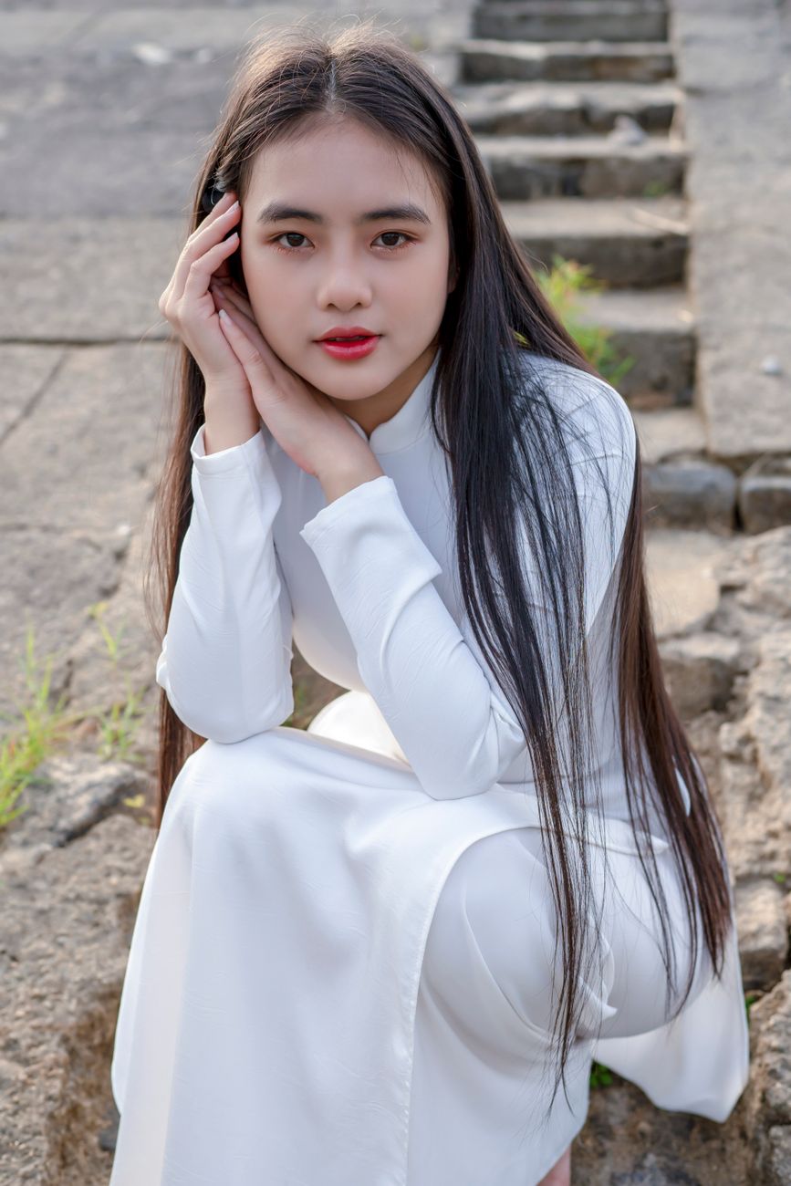 Portrait of a woman wearing a traditional white dress, sitting outdoors.