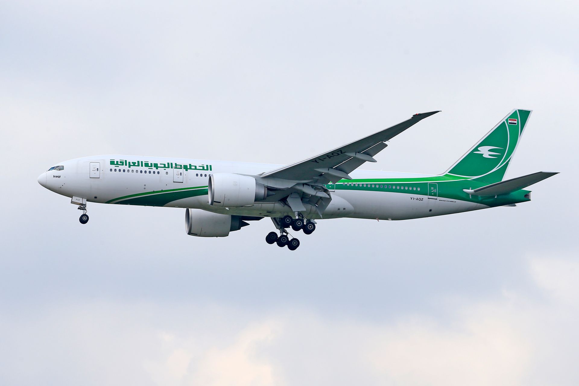 Iraqi Airways Boeing 777 flying with landing gear down against a cloudy sky, showcasing the airline's signature green livery.