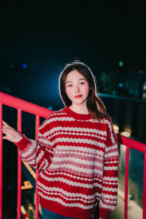 A young woman in a red sweater standing on a balcony