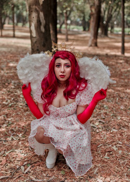 A woman with red hair and wings sitting in the woods