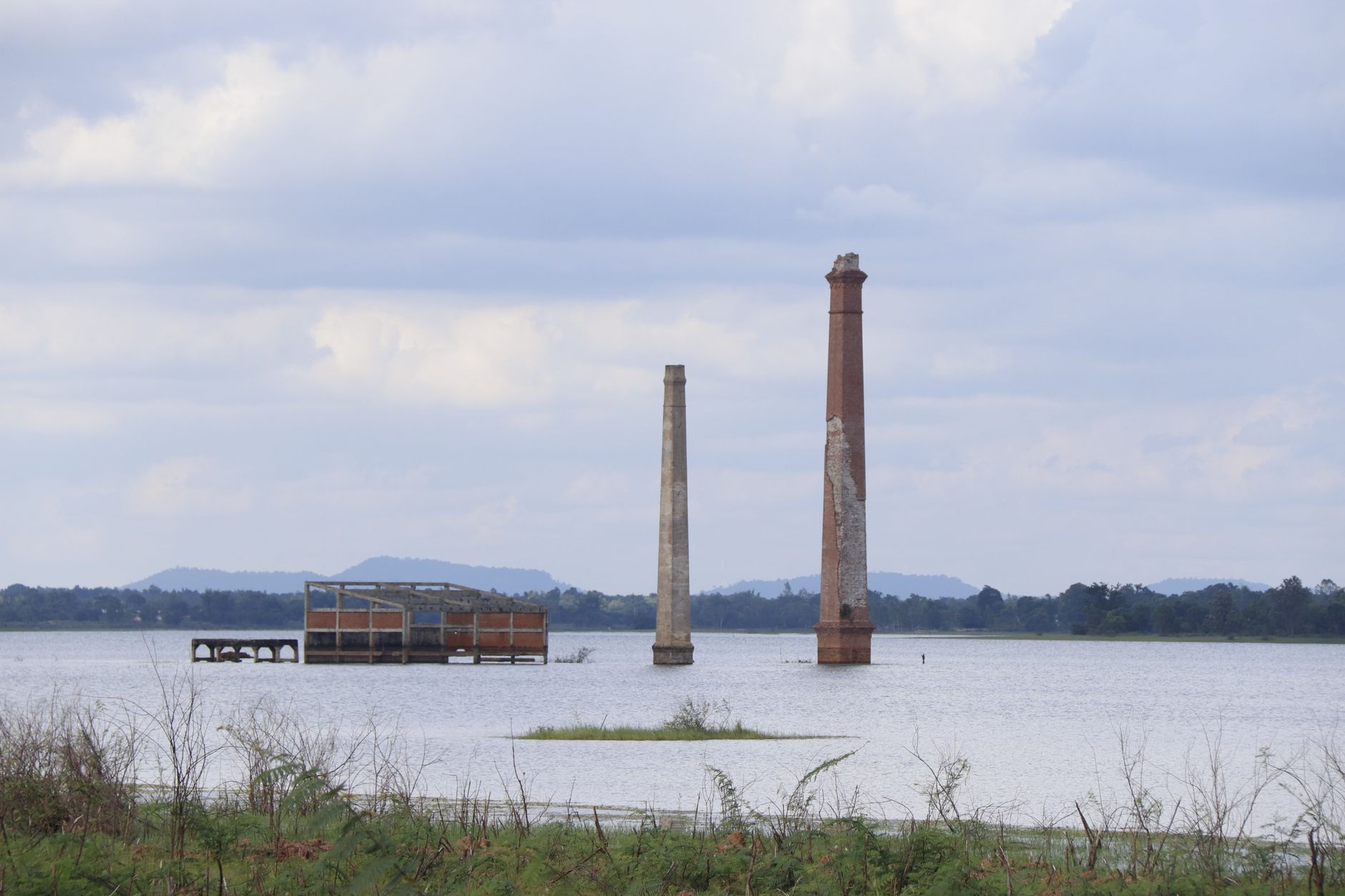 A view of two abandoned chimneys rising from a flooded reservoir under a cloudy sky.