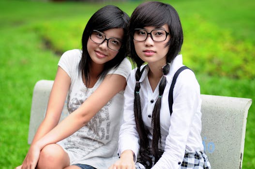 Two young women with glasses smiling while sitting on a park bench.