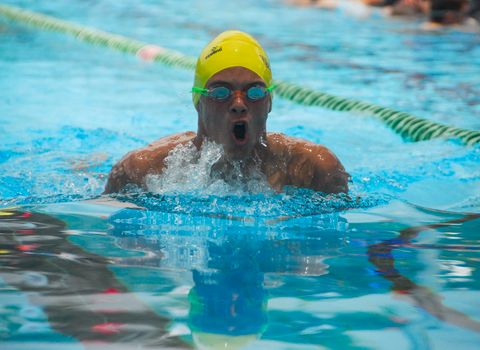Swimmer competes with intensity in a sunny outdoor pool setting.