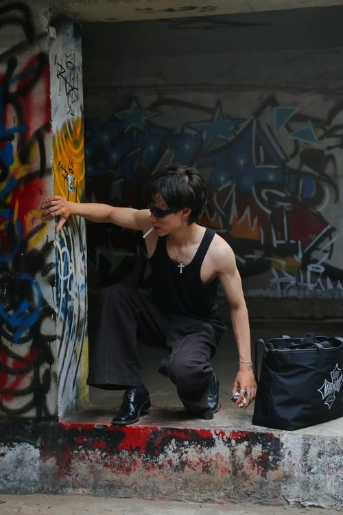 Free A street artist in sunglasses and black top crouches by vibrant graffiti artwork. Stock Photo