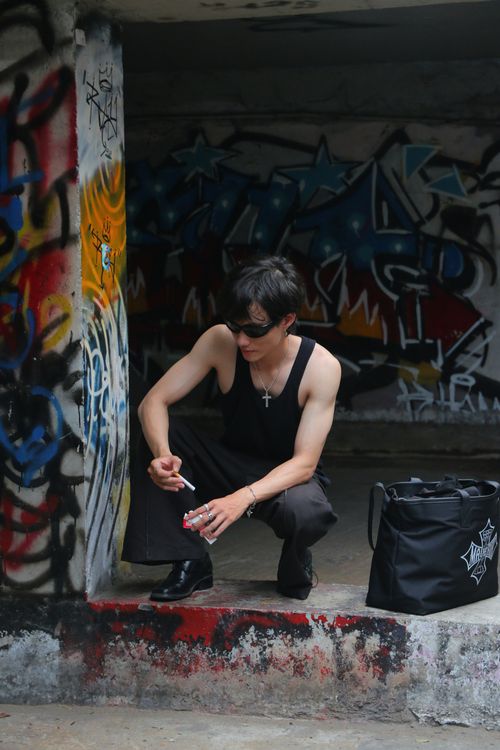 Free Young man squatting by a graffiti wall holding a cigarette in an urban setting. Stock Photo