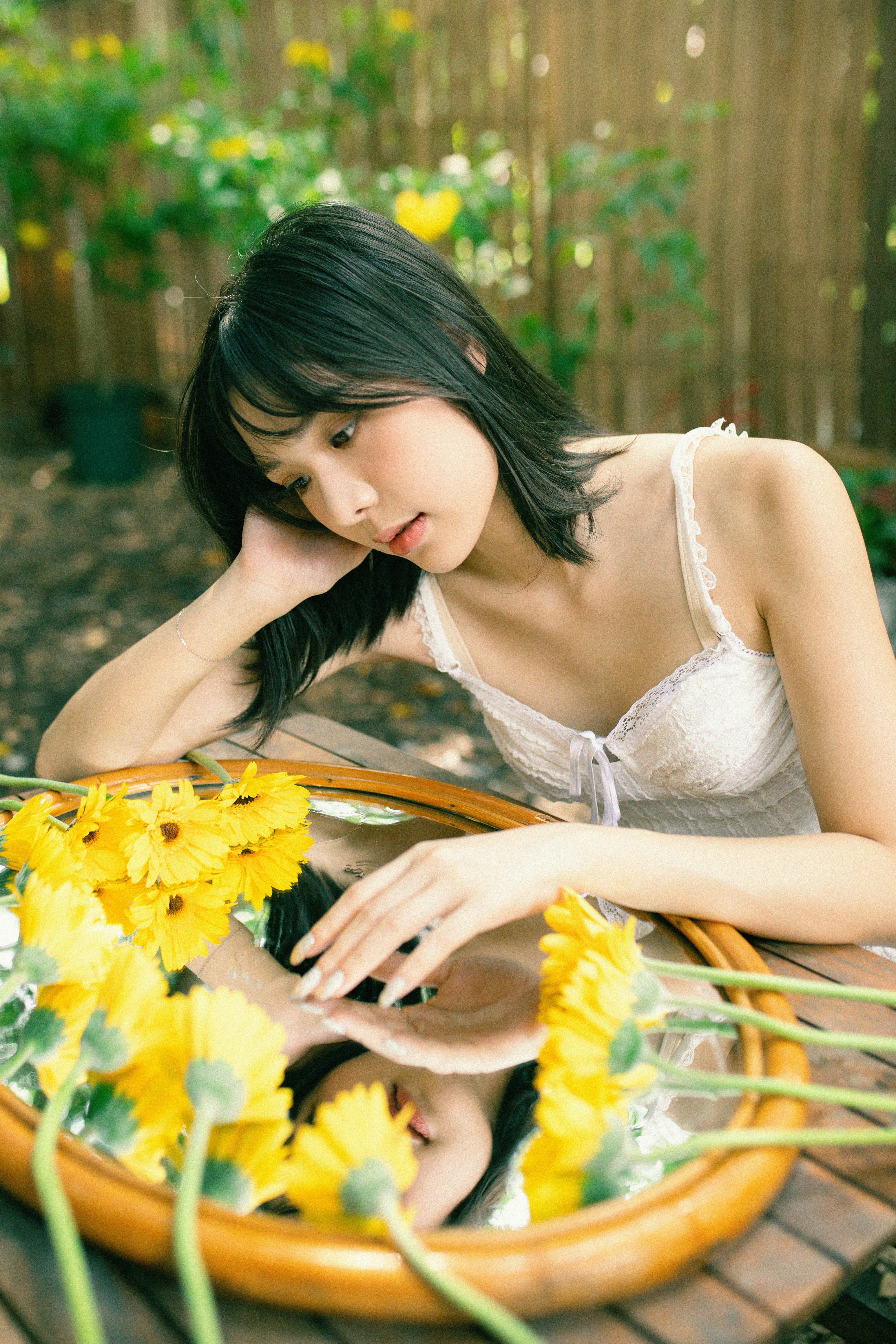 Woman in a garden admiring her reflection in a mirror surrounded by yellow flowers.