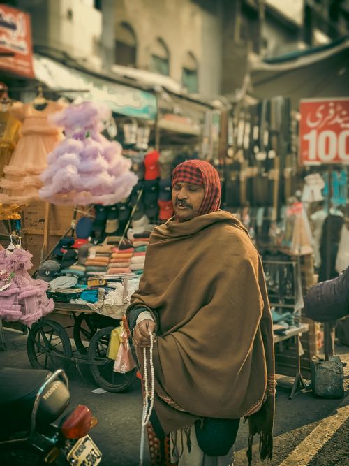 Free Portrait of a man wrapped in a blanket amidst a bustling street market showcasing textiles and cotton candy. Stock Photo