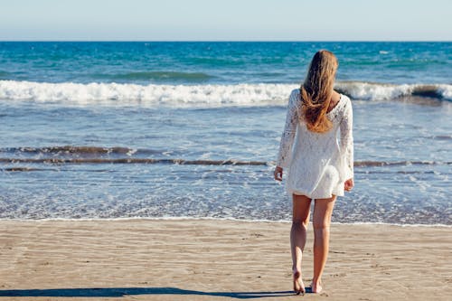 站在海邊的白色蕾絲長袖迷你連衣裙的棕髮女人