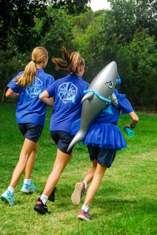 一個女孩背著鯊魚氣球和兩個穿著藍色制服的女孩跑