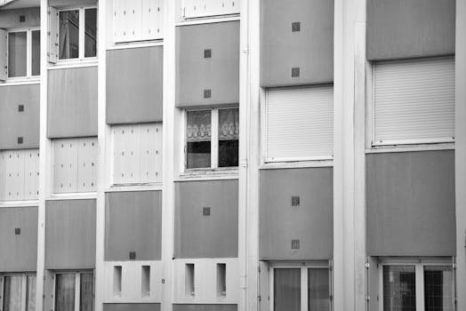 Black and white photo of apartment facade with repetitive window pattern.