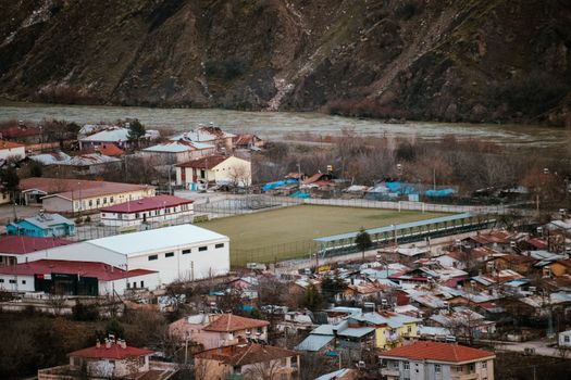 A scenic aerial view of a town with a soccer field in Palu, Elazığ, Türkiye, surrounded by mountains.