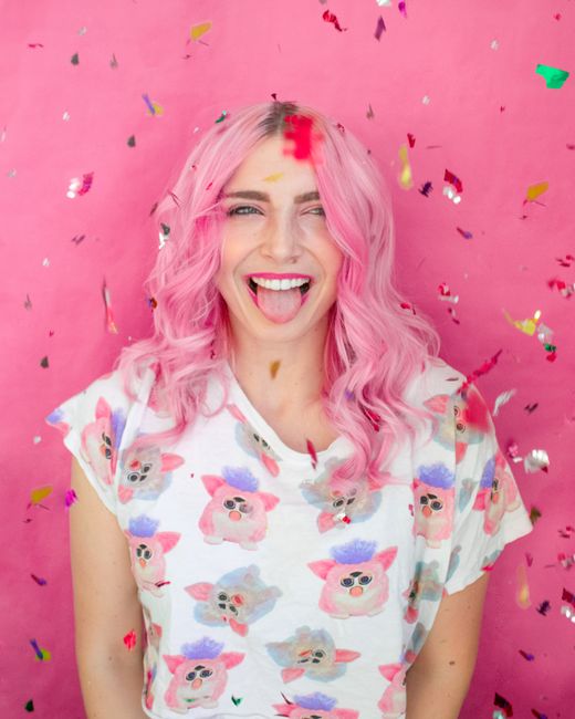 Cheerful woman with pink hair and fun confetti accents on a vibrant pink backdrop.