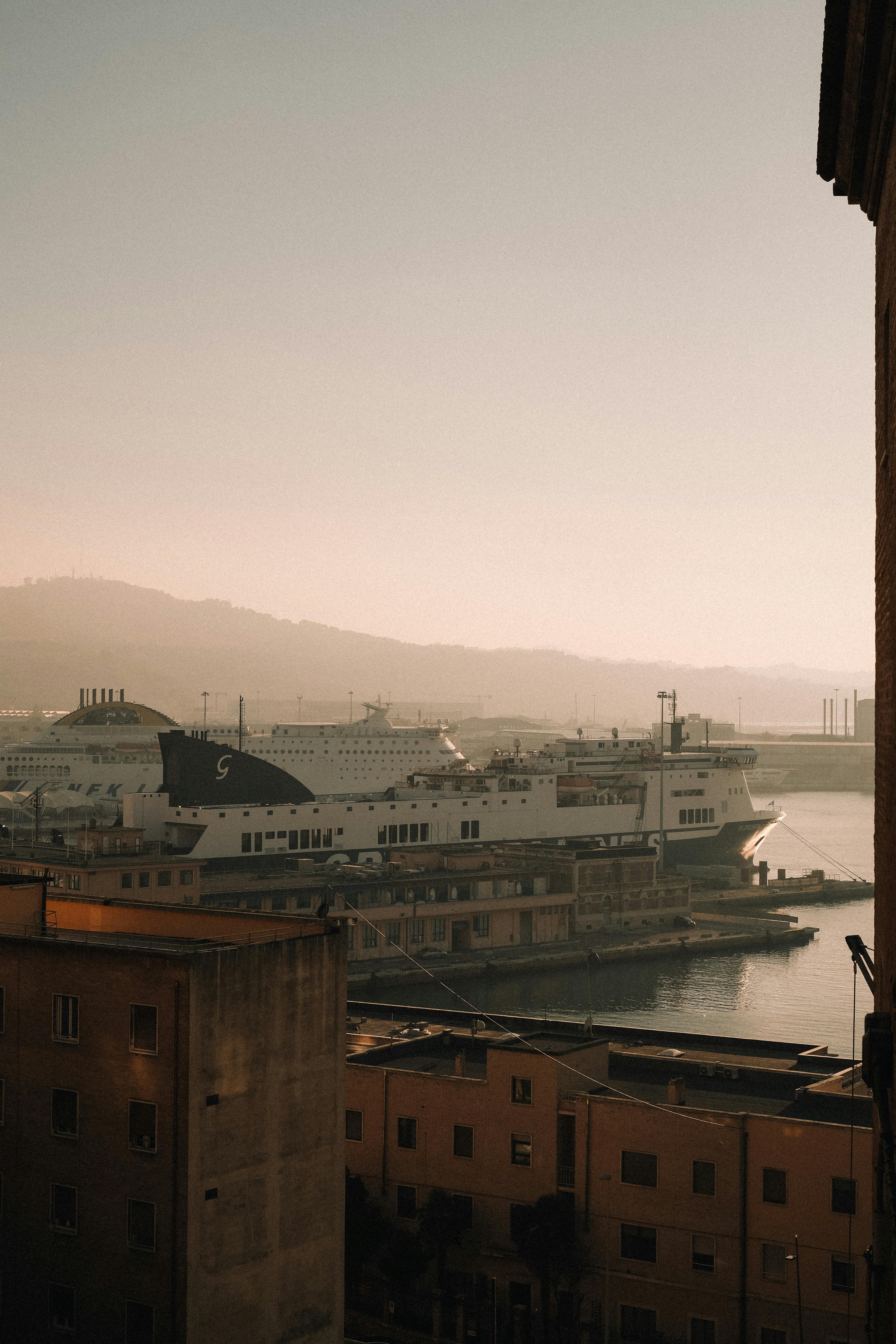 A serene view of ferries docked at a misty harbor during sunrise, with hills in the background.