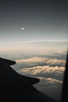 Dramatic aerial view of mountains under moonlit sky from an airplane window.
