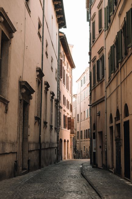 A narrow, empty Italian alleyway with cobblestones and classic architecture under warm sunlight.