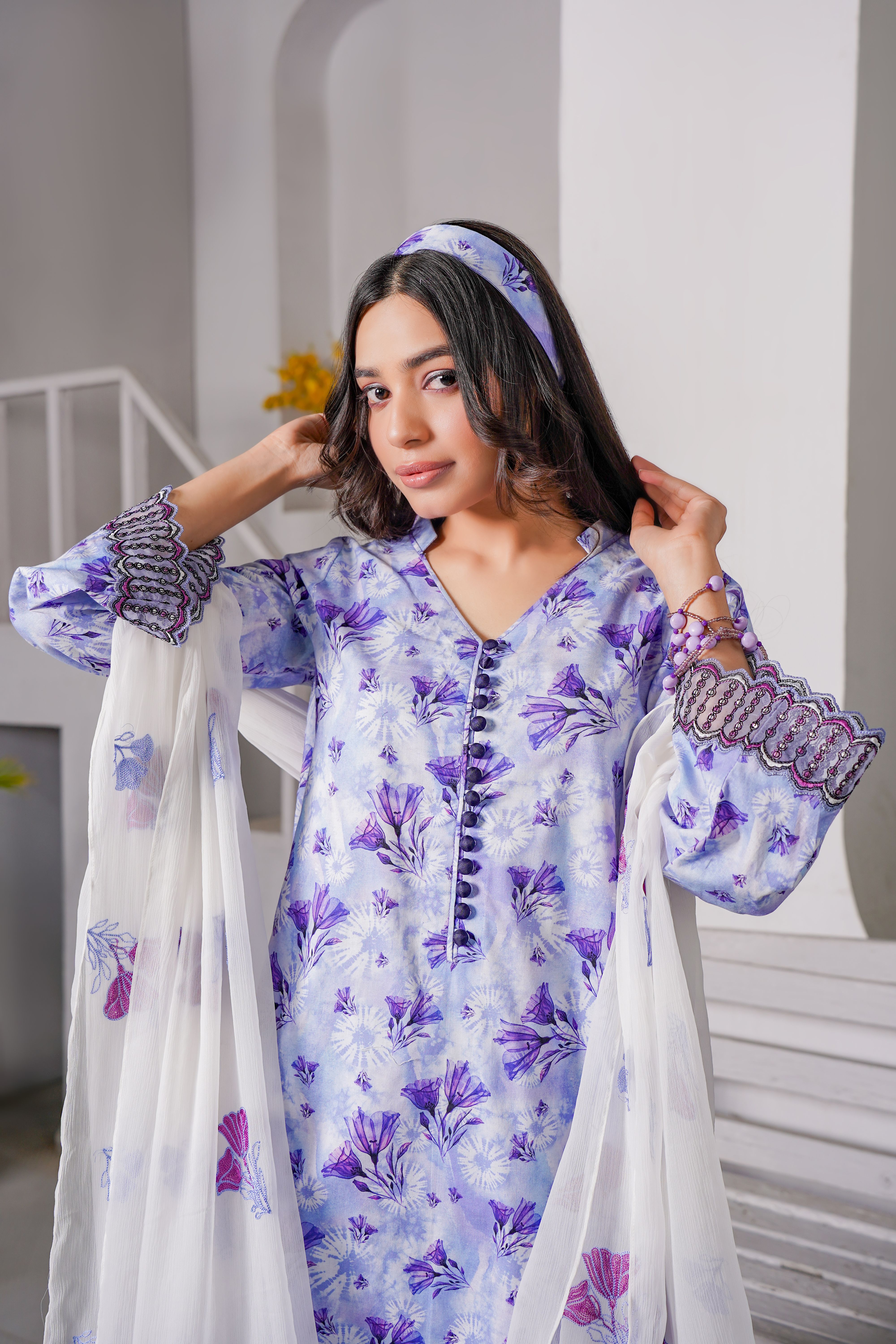 Beautiful woman in floral lavender dress with white scarf, posing indoors for fashion photography.