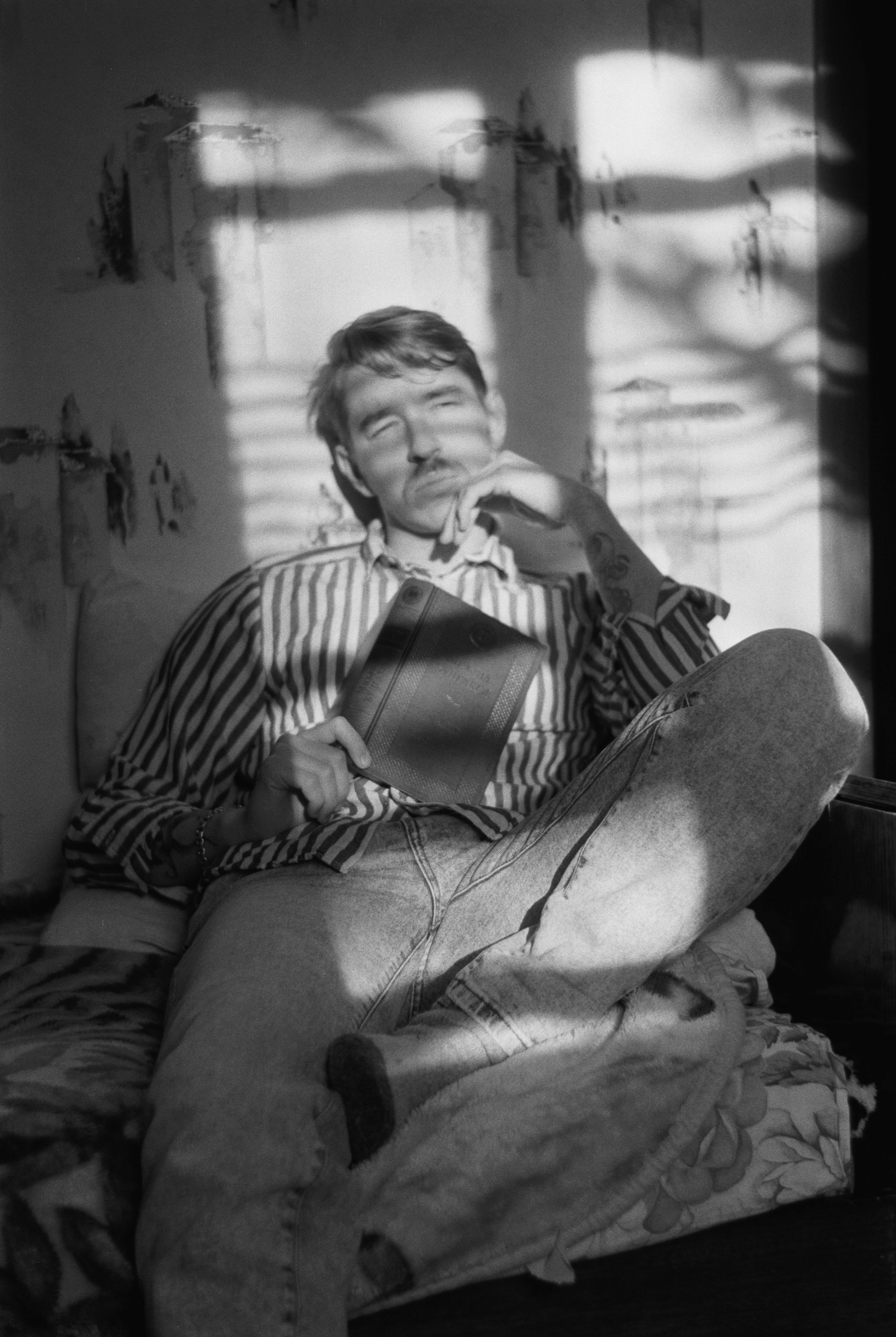 Black and white portrait of a man sitting with a book, thoughtful and relaxed indoors.