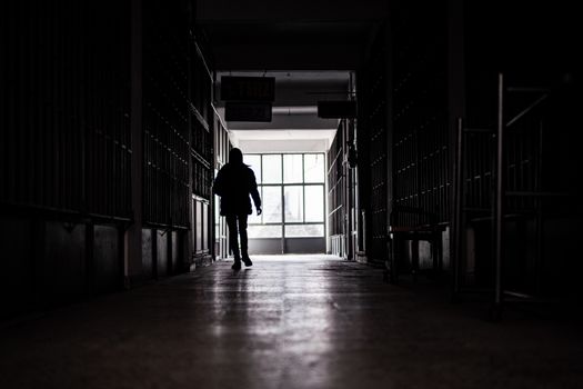 A lone silhouette of a man walking through a dark, shadowy hall towards light.