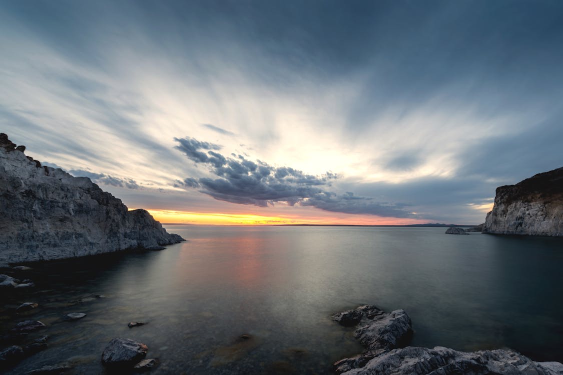 A sunset over the ocean with rocks and clouds