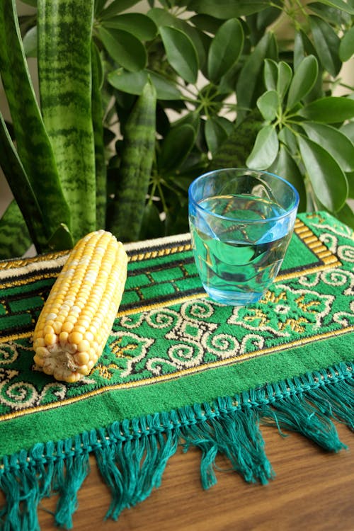 A corn on a table next to a glass of water
