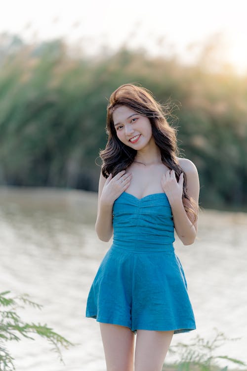 A beautiful young woman in blue dress posing near water